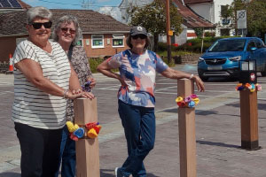 Three women standing in front of bollards with knitted flowers on 